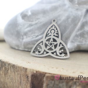 Könnte beinhalten: Silberner Anhänger-Anhänger mit einem Triquetra-Design mit Stern-, Mond- und Sonnensymbolen. Der Anhänger ist aus Metall und hat eine glänzende Oberfläche.