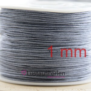 Könnte beinhalten: Eine Spule mit 1 mm grau gewachstem Kordel. Die Kordel ist fest um die Spule gewickelt und bildet eine glatte, gleichmäßige Oberfläche. Die Spule besteht aus weißem Kunststoff und trägt ein Etikett mit der Aufschrift "LustaaufPerlen".