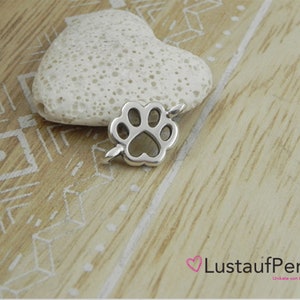 May include: Silver charm in the shape of a paw print. The charm is on a white heart-shaped rock.