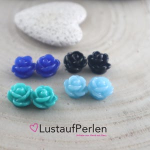 Könnte beinhalten: Sortiment kleiner rosenförmiger Harzembellen in verschiedenen Farben, darunter Blau, Türkis, Schwarz und Hellblau.