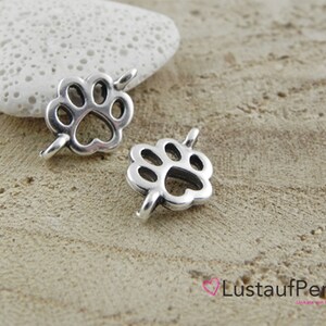 May include: Two silver metal paw print charms with a hole for attaching to a necklace or bracelet.