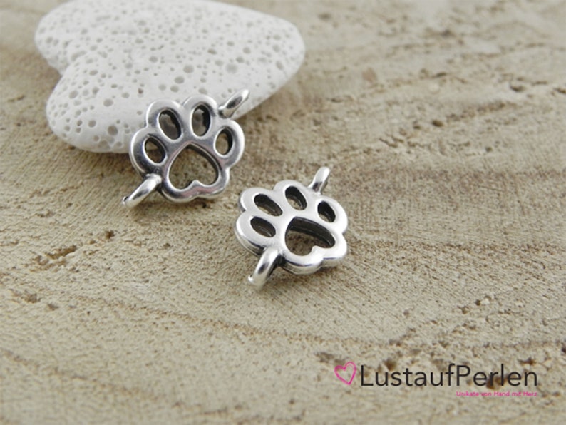 May include: Two silver metal paw print charms with a hole for attaching to a necklace or bracelet.