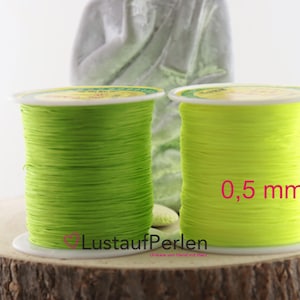 Könnte beinhalten: Zwei Spulen neongrünes Schmuckfaden, jeweils eng auf eine weiße Kunststoffspule gewickelt. Eine Spule ist dunkler grün, die andere ein helleres, fast gelbes Grün. Der Text "0,5 mm" ist auf einer Spule sichtbar.