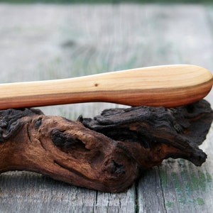 Könnte beinhalten: Ein Holzbuttermesser mit natürlicher Holzoptik. Das Messer liegt auf einem Stück Treibholz.