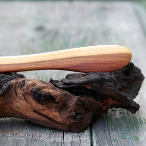 Könnte beinhalten: Ein Holzbuttermesser mit natürlicher Holzmaserung, das auf einem Stück Treibholz liegt.