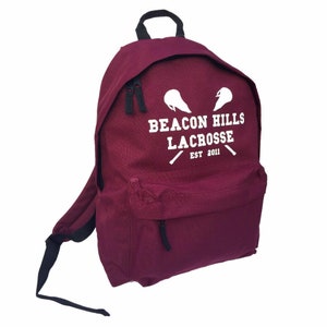 Op de afbeelding: Bordeauxrode rugzak met een wit logo met de tekst "Beacon Hills Lacrosse Est 2011" met twee gekruiste lacrosse-sticks.