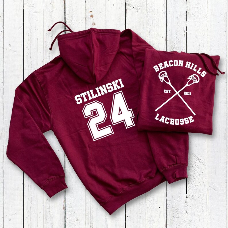 May include: Burgundy hooded sweatshirt with white text "Stilinski 24" on the back. A second burgundy hooded sweatshirt with white text "Beacon Hills Est. 2011 Lacrosse" on the front.