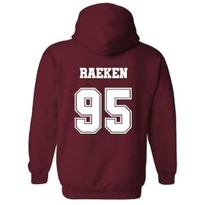 Pode incluir: Camisola de capuz cor vinho com o nome "Raeken" e o n&uacute;mero "95" impressos em branco nas costas.