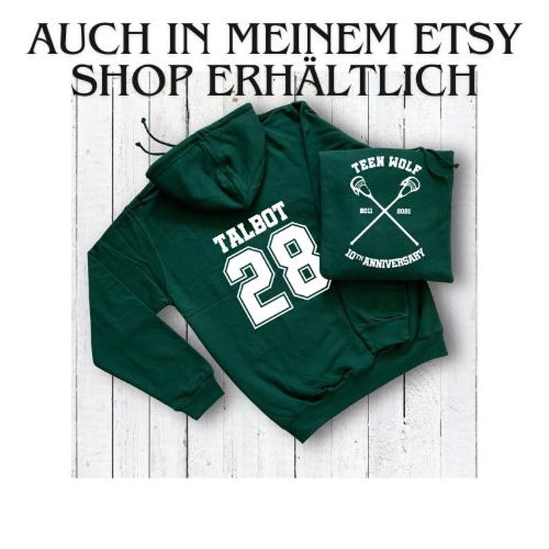 Pode incluir: Camisola de capuz verde com o texto "TALBOT 28" impresso nas costas em branco. Um remendo branco menor com o texto "TEEN WOLF 10TH ANNIVERSARY" est&aacute; preso na frente da camisola.