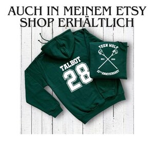 May include: Green hooded sweatshirt with the text "TALBOT 28" printed on the back in white. A smaller white patch with the text "TEEN WOLF 10TH ANNIVERSARY" is attached to the front of the sweatshirt.