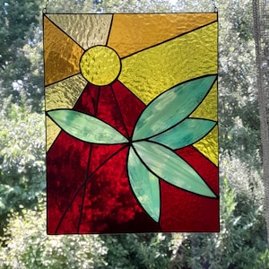 Peut inclure: Un panneau de vitrail avec un motif abstrait rouge, jaune et vert. Le motif représente un soleil stylisé avec des rayons et une forme de feuille.
