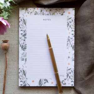 May include: A white notepad with a floral border and the word "NOTES" printed at the top. A gold pen is lying on the notepad.