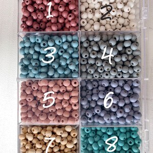 May include: Eight containers of wooden beads in various colors, including dusty rose, white, light blue, gray, blush pink, lavender, beige, and teal. Each container is labeled with a number from 1 to 8.