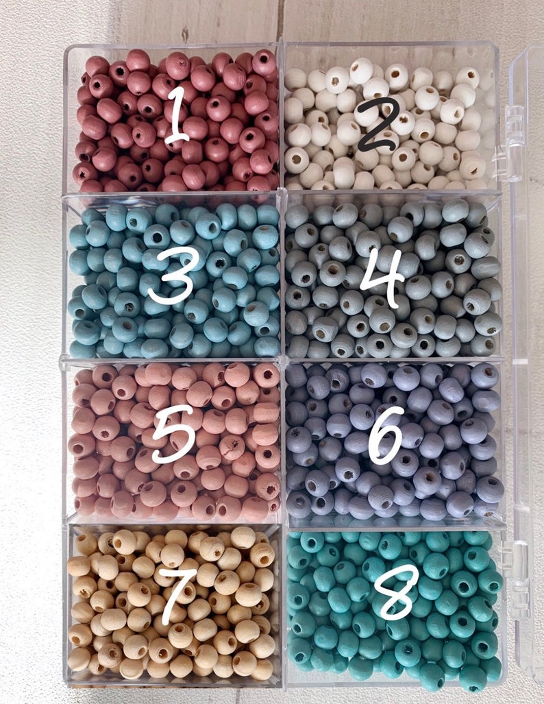 May include: Eight containers of wooden beads in various colors, including dusty rose, white, light blue, gray, blush pink, lavender, beige, and teal. Each container is labeled with a number from 1 to 8.