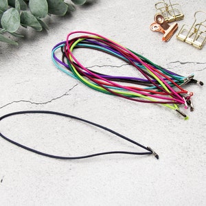 Puede incluir: Una colección de cordones elásticos de colores con cierres metálicos. Los cordones están dispuestos en forma de abanico y están listos para ser utilizados para manualidades o la elaboración de joyas.