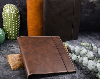 May include: Three rectangular portfolios with smooth, textured covers in shades of tan, dark brown, and medium brown. Each portfolio features a vertical elastic band closure and visible stitching along the edges, presenting a clean, structured design.