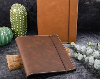 May include: Two rectangular folders with elastic closures. One folder is light tan, and the other is a darker brown. Both feature visible white stitching along the edges and a smooth, matte finish. The folders are positioned upright and angled.