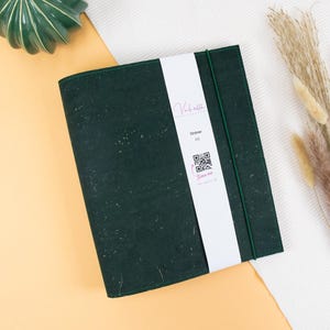 May include: A dark green cork binder with a white label that says "Ordner A5" and has a QR code. The label also has the text "Vachatta" in pink lettering.