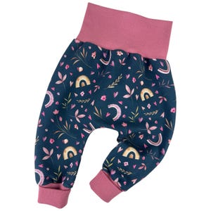 Puede incluir: Pantalones de bebé azul y rosa con estampado y cintura elástica rosa. El estampado presenta pequeñas flores, hojas y arcoíris.