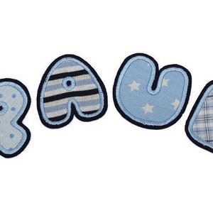 Könnte beinhalten: Ein blaues und weißes Stoff-Namensbanner mit dem Wort "PAUL" in großen, bunten Buchstaben. Jeder Buchstabe hat ein anderes Muster, darunter Punkte, Streifen, Sterne und Karos.