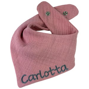 以下が含まれることがあります： ピンクのバンダーナよだれかけ。スナップ留めと、グレーの糸で「Carlotta」という名前が刺繍されています。