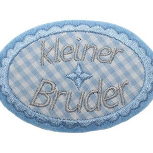 Könnte beinhalten: Ein blauer und weißer kariertes ovaler Patch mit einem weißen gewellten Rand. Der Patch ist mit dem Text "kleiner Bruder" in silbernem Faden bestickt.