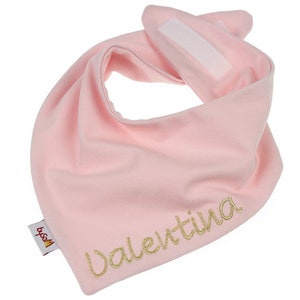 May include: Pink baby bandana bib with a gold embroidered name "Valentina" and a small red and yellow logo that says "byssa".