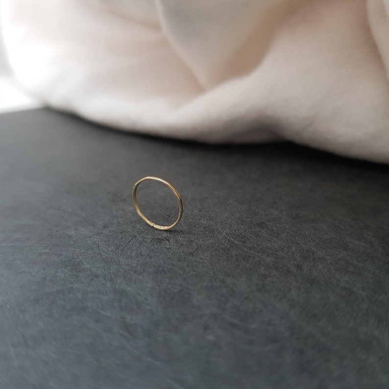 May include: A thin gold band ring, lying on a dark gray surface.