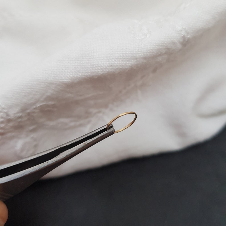May include: A pair of silver tweezers holding a small, thin, gold ring.