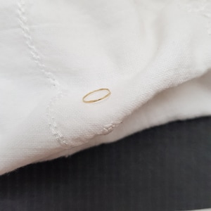 May include: A thin gold ring on a white fabric background.
