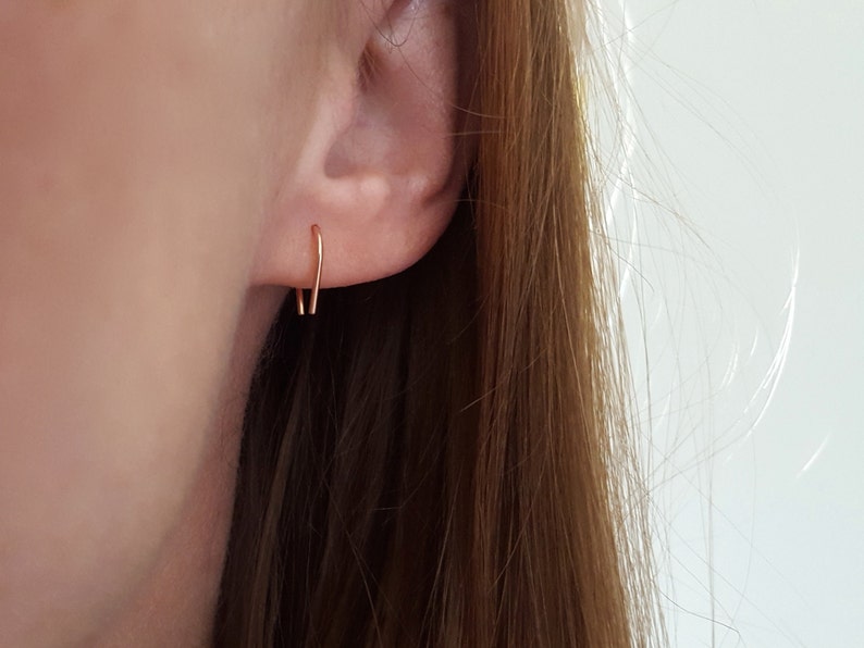 Pu&ograve; includere: Un paio di piccoli orecchini a cerchio d'oro semplici. Gli orecchini sono sottili e delicati e sono mostrati indossati in un orecchio.