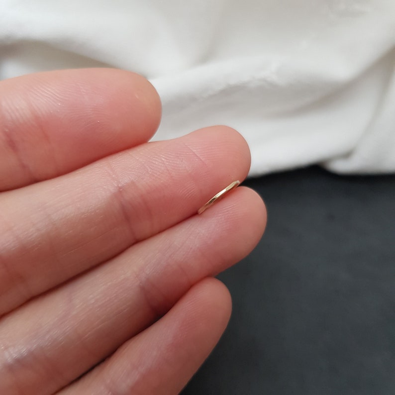 May include: A thin gold hoop earring, shown on a finger.