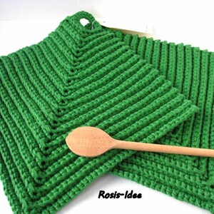 Könnte beinhalten: Zwei grüne, quadratische, gehäkelte Topflappen mit einem Holzlöffel. Die Topflappen haben eine gerippte Textur und eine Schlaufe zum Aufhängen. Der Löffel ist hellbraun und liegt auf den Topflappen. Der Text "Rosis-Idee" steht unten rechts.
