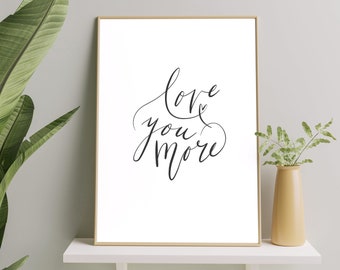May include: A black and white printable wall art print with the text "Love you more" in a cursive font.