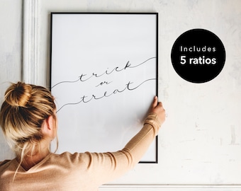 May include: A black framed print with the text "trick or treat" in a handwritten font. The print is hanging on a white wall.