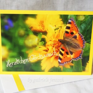 Könnte beinhalten: Eine gelbe Glückwunschkarte mit einer gelben Blume und einem Schmetterling. Die Karte trägt den Text "Herzlichen Glückwunsch".