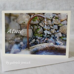 May include: A greeting card with a photograph of a stone wall and a water fountain. The card has the words "Atme und lass sein!" and "Jon Kabat-Zinn" printed on it. The card is on top of a white envelope with the words "by gabriele jentsch" printed on it.