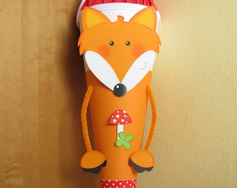 May include: Orange cone-shaped gift bag with a fox face design. The fox has white and orange features, black eyes, and a black nose. The bag has orange pipe cleaner arms and feet. A mushroom and flower are on the front.