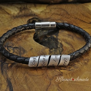 Può includere: Braccialetto in pelle nera con chiusura magnetica e cinque perline d'argento incise con i nomi "Karl", "Otta", "Leo" e "Erik".