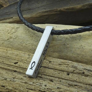 Könnte beinhalten: Eine silberne Anhänger-Halskette mit einem schwarzen Lederband. Der Anhänger ist rechteckig und mit dem Text "Psalm 10:11" und einem Fischsymbol graviert.