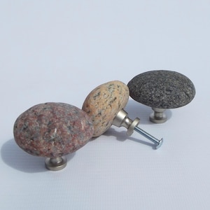Könnte beinhalten: Drei Schrankknöpfe aus Naturstein in Rot-, Beige- und Grautönen. Jeder Knopf hat einen Sockel aus gebürstetem Nickel und eine Schraube zur Befestigung. Die Knöpfe sind oval geformt und haben eine glatte, polierte Oberfläche.