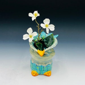 May include: A ceramic vase shaped like a bird with blue and yellow accents. The vase is filled with white flowers and green leaves.