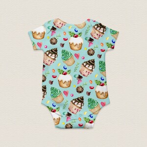 May include: A light blue baby onesie with a pattern of cupcakes, candy, and green leaves. The cupcakes are decorated with chocolate frosting, sprinkles, and cherries.