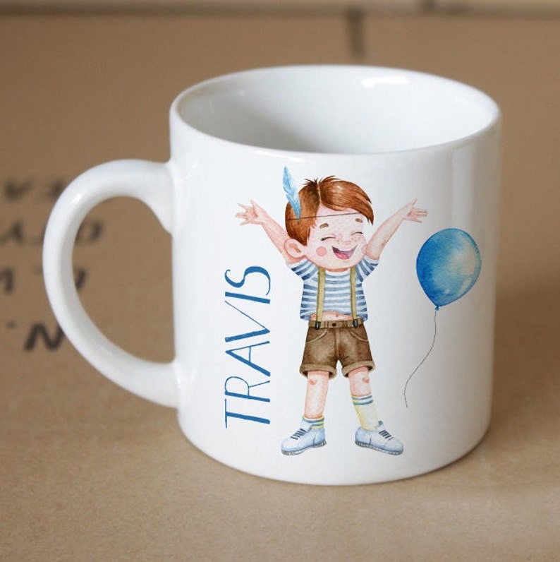 Pode incluir: Caneca de cer&acirc;mica branca com uma ilustra&ccedil;&atilde;o azul e marrom de um menino segurando um bal&atilde;o azul. O texto "TRAVIS" est&aacute; impresso na caneca.