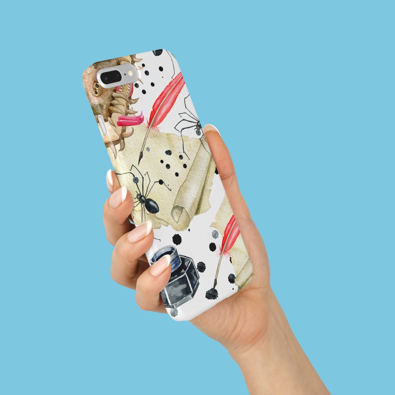 May include: A white phone case featuring a watercolor design with black ink splatters, antique scrolls, red quill pens, and black spiders. The case also includes a black inkwell and a small, brown object.