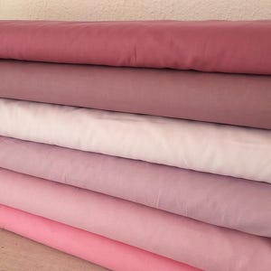 Può includere: Una pila di tessuti in varie tonalità di rosa e viola. I colori vanno da un rosa intenso a un lavanda chiaro, creando un effetto sfumato. Il tessuto sembra morbido e liscio, adatto per progetti di cucito.