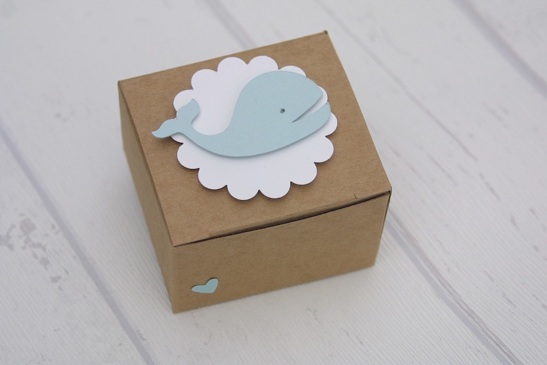May include: A small brown cardboard box with a white scalloped circle and a light blue whale cutout on top. A small light blue heart is on the side of the box.