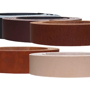 Può includere: Una collezione di strisce di cuoio in vari colori, tra cui nero, marrone scuro, marrone medio, marrone rossiccio e beige. Le strisce arrotolate mostrano la consistenza e le variazioni di colore della pelle.