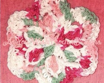May include: A handmade crochet flower in shades of white, pink, and green, set against a pink background. The flower has a detailed, textured design, with a scalloped edge. The craftwork is likely a coaster or decorative item.