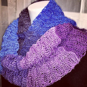 May include: A handmade infinity scarf in shades of blue and purple. The scarf is crocheted with a textured stitch, creating a visually interesting pattern. The yarn has a subtle sparkle, adding a touch of elegance to the accessory.